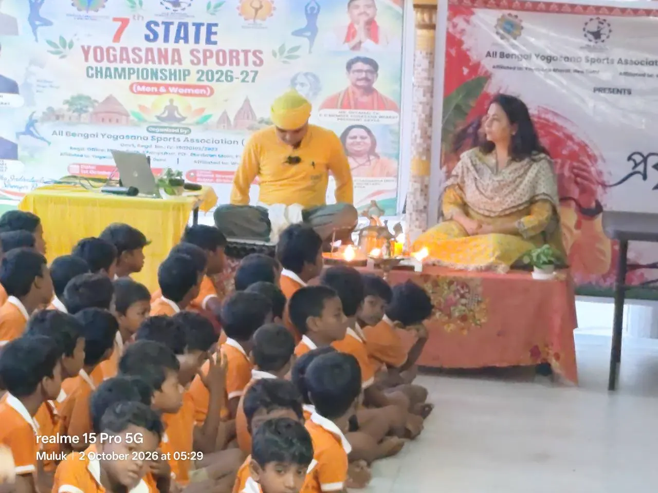 Children in orange sit in the hall.