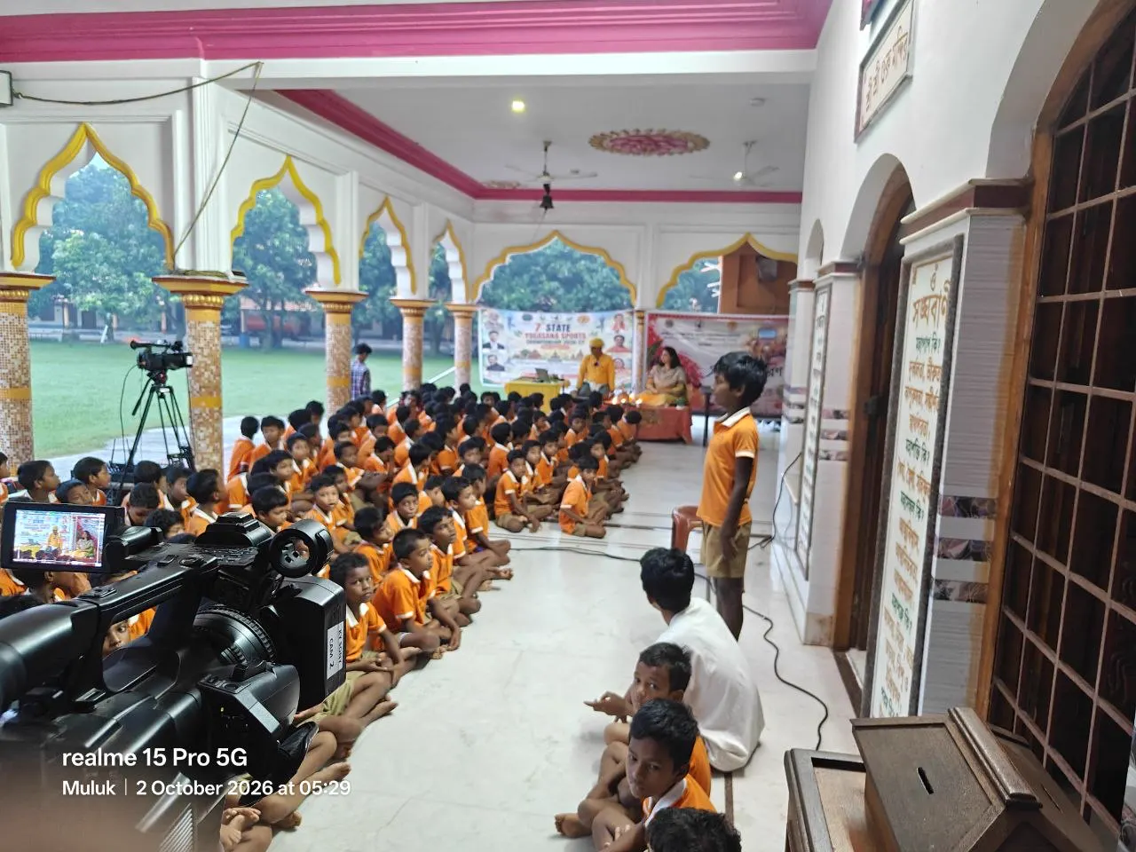 Young athletes in orange sit along the mandir verandah.