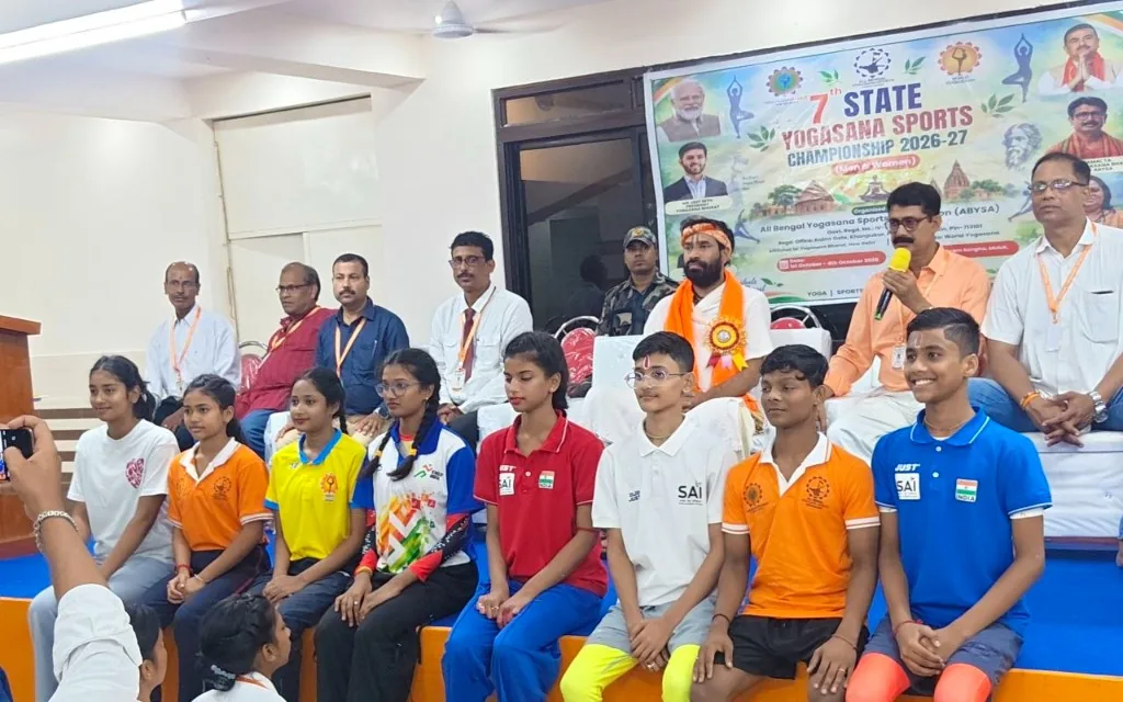Young athletes seated in rows during an indoor championship session, with officials behind them.