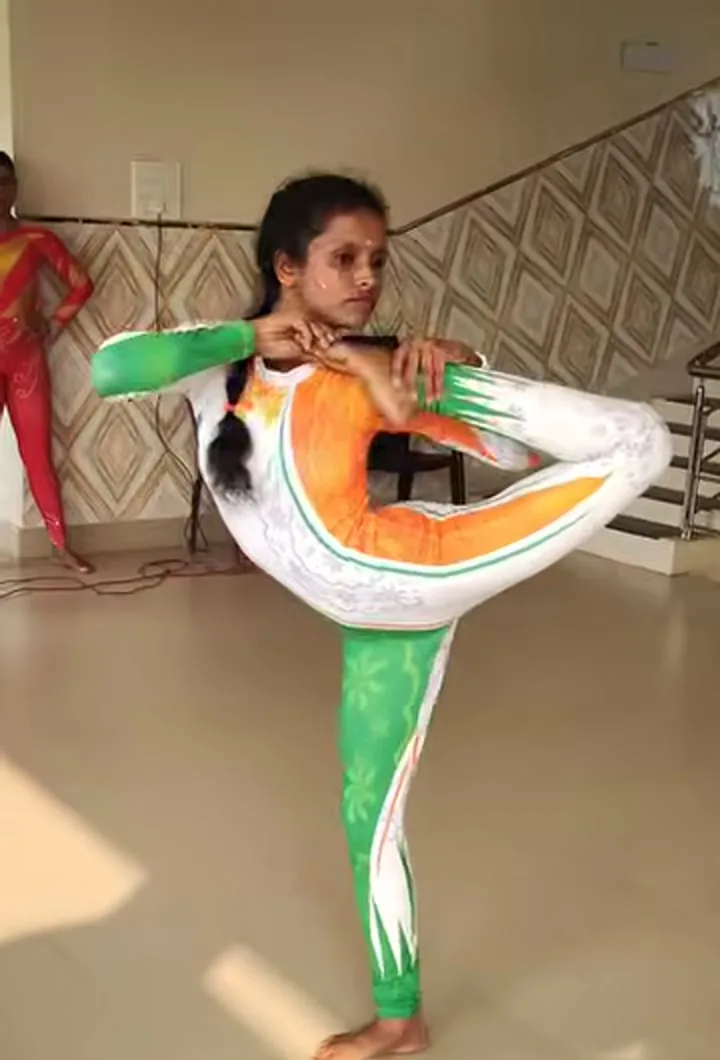 An athlete in a green, white and orange suit holds a standing balance, one foot drawn up behind the head, during an artistic-pair step.