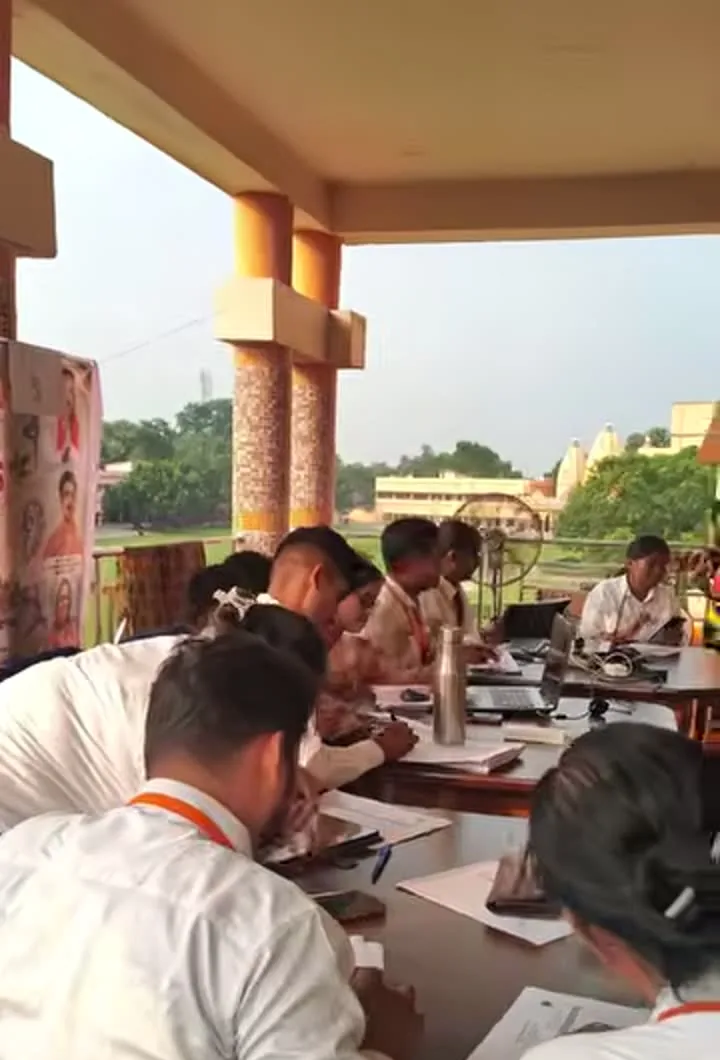 Judges seated at a long table on the verandah, entering marks on papers beside laptops.